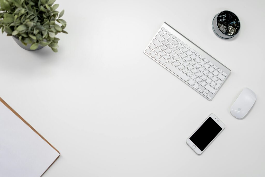 A neat and organized home office setup with a wireless keyboard, mouse, and smartphone.